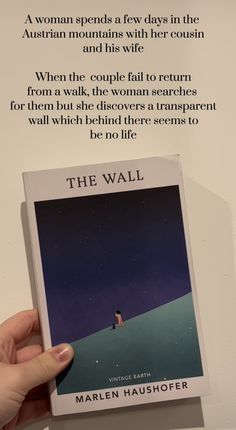 a person holding up a book about the wall by marilyn haushoffer, which is in front of a white background