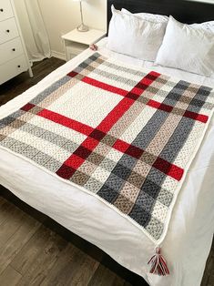 a white bed topped with a red and gray plaid blanket next to a night stand