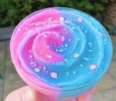 a hand holding up a pink and blue cup with sprinkles on it