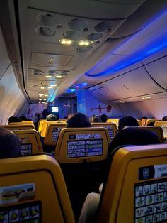 the inside of an airplane with rows of seats and televisions on each side of the aisle