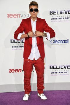 a man in a red suit and sunglasses standing on a purple carpet with his arms crossed