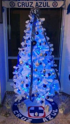 a white christmas tree with blue lights in front of a window and sign that says cruz azul