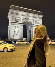 a woman is standing in front of the arc de trioe triumph gate at night