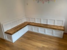 an empty room with white paneling and wooden bench in the corner, on hard wood flooring