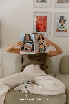 a woman sitting on a couch holding up a magazine in front of her face and looking at the camera