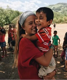 two children hugging each other in the middle of an open field with people around them