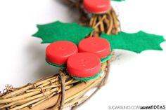 some red buttons are sitting on top of a wicker wreath with holly leaves and green felt