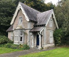 an old stone house in the middle of some trees and grass with bushes around it