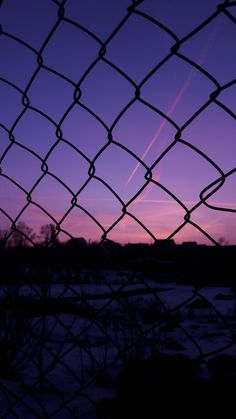 an airplane is flying in the sky behind a chain link fence at sunset or dawn