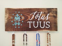 a wooden sign that says tous tuus hanging on a wall with several bracelets