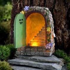 a small green door sitting on top of a rock next to a tree and grass