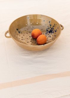 three oranges in a bowl on a table with a blue and white striped napkin