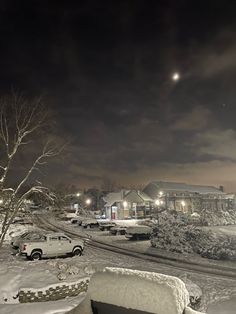 cars parked on the side of a road covered in snow at night with street lights