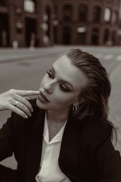 a woman sitting on the ground in front of a building with her hand under her chin