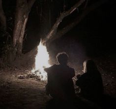 two people sitting around a campfire at night