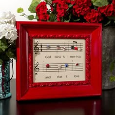 a red frame with music notes and flowers in the vase next to it on a table