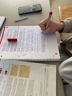 a person sitting at a table writing on a piece of paper with a red pen