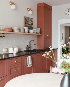 a kitchen with red cabinets and white counter tops, along with a clock on the wall