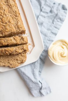 sliced oatmeal bread on a white plate next to a bowl of yogurt