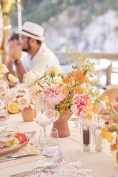 two men are sitting at a table with flowers in vases and plates on it