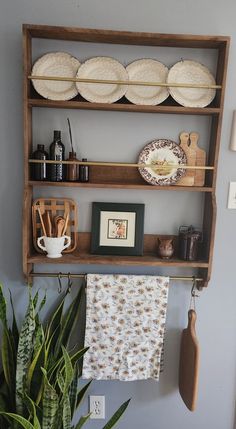 a wooden shelf with plates and utensils on it next to a potted plant