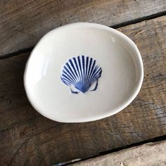 a white bowl with a blue shell painted on the side sitting on a wooden table