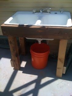 an orange bucket sitting on top of a wooden table next to a metal sink and toilet