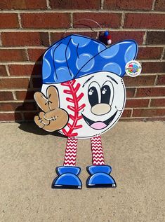 a blue and white baseball mascot standing in front of a brick wall on the sidewalk