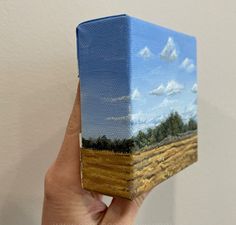 a hand holding up a small box with a painting on it