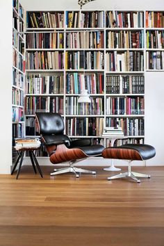 two chairs and a table in front of a bookshelf with many books on it