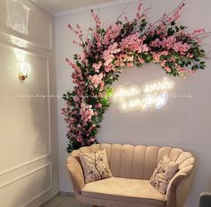 a couch sitting in front of a wall with pink flowers and greenery on it