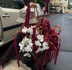 a woman sitting on the ground next to a car with flowers in front of her