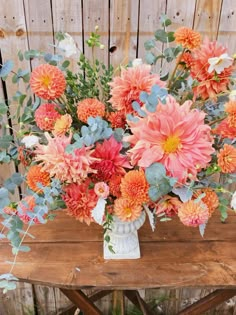 a vase filled with lots of flowers on top of a wooden table next to a fence