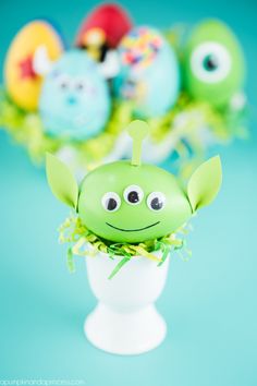 a green plant with googly eyes in a white vase filled with fake plants and eggs