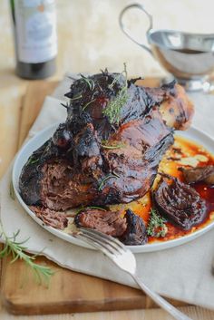 a white plate topped with meat covered in sauce next to a knife and fork on top of a wooden cutting board