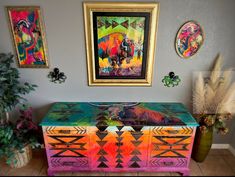 a colorful painted dresser in the corner of a room with paintings on the wall and potted plants