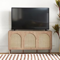 a flat screen tv sitting on top of a wooden cabinet next to a potted plant