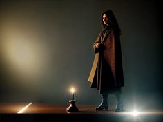 a woman standing in front of a lit candle on a wooden table with a dark background