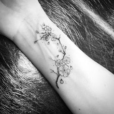 a black and white photo of a cherry blossom tattoo on the left arm, with water droplets running down it