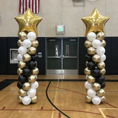 two tall gold and white balloons in the middle of a gym with an american flag