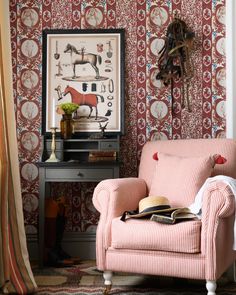 a pink chair sitting in front of a wall with a clock on top of it