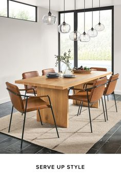 a dining room table with chairs and lights hanging from it's ceiling, in front of a large window