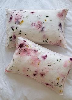 two pillows that have been dyed with different colored dyes on them sitting on a bed