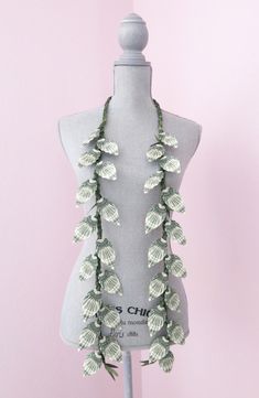 a white mannequin with green leaves on it's neck and two necklaces