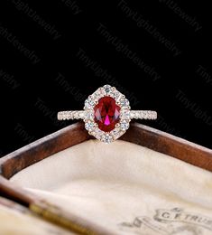 a ring with a red stone surrounded by white diamonds in a wooden box on a black background