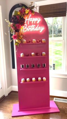 a pink display case with cupcakes and candles on it in front of a window