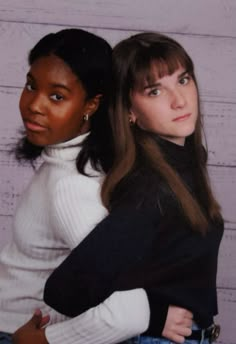 two women standing next to each other in front of a wall