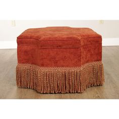 an orange ottoman with fringe trim on the top and bottom, sitting on a wooden floor