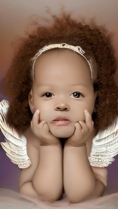 a baby girl with angel wings on her head and hands under her chin, looking at the camera