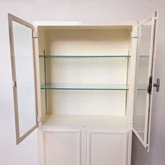 an empty white cabinet with glass shelves in the front and side doors on both sides